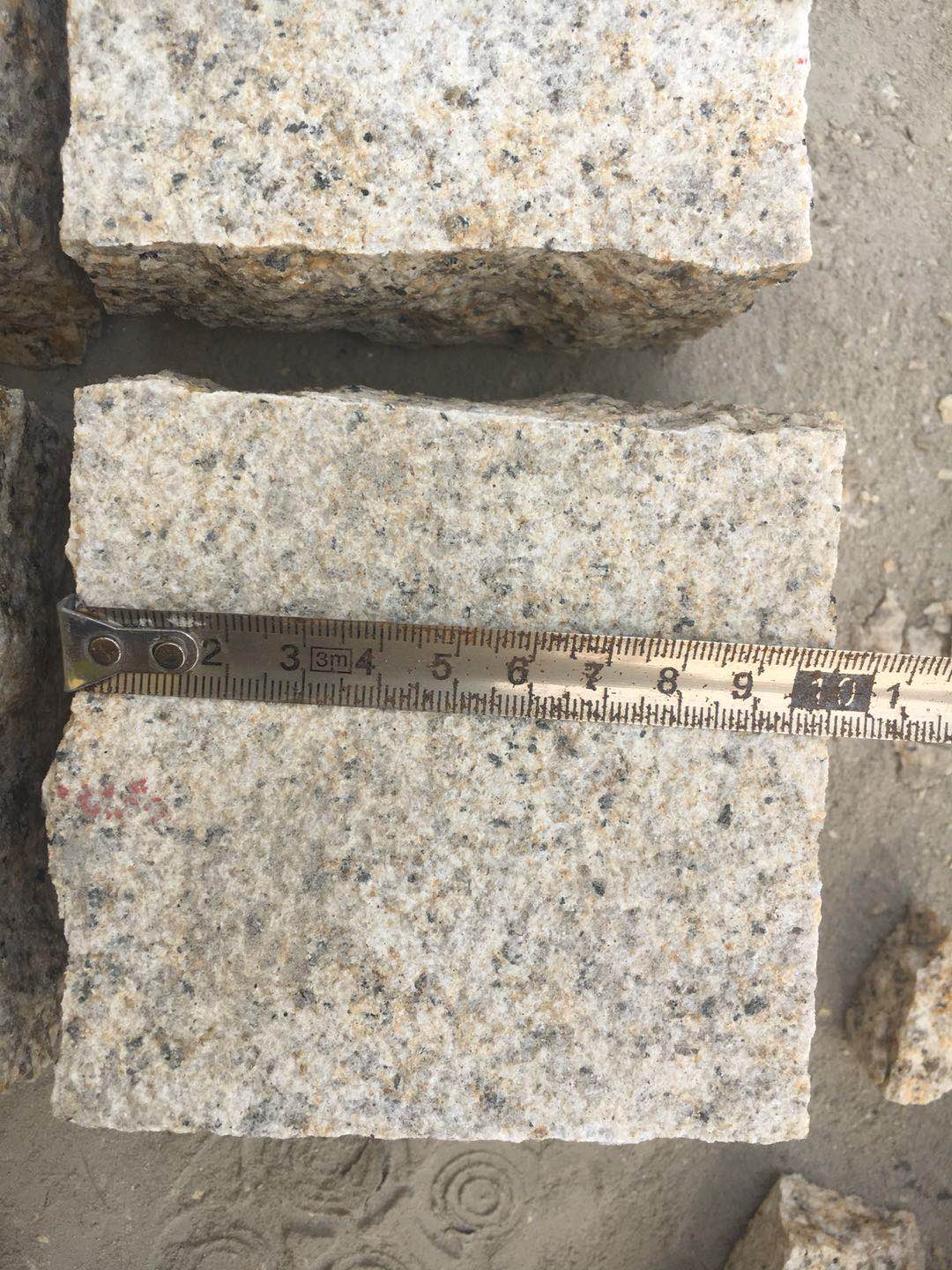 Natural Split Yellow Granite Cobble Stone Granite — Measuring cobble width with a tape measure during quality control at Sun Young Stone