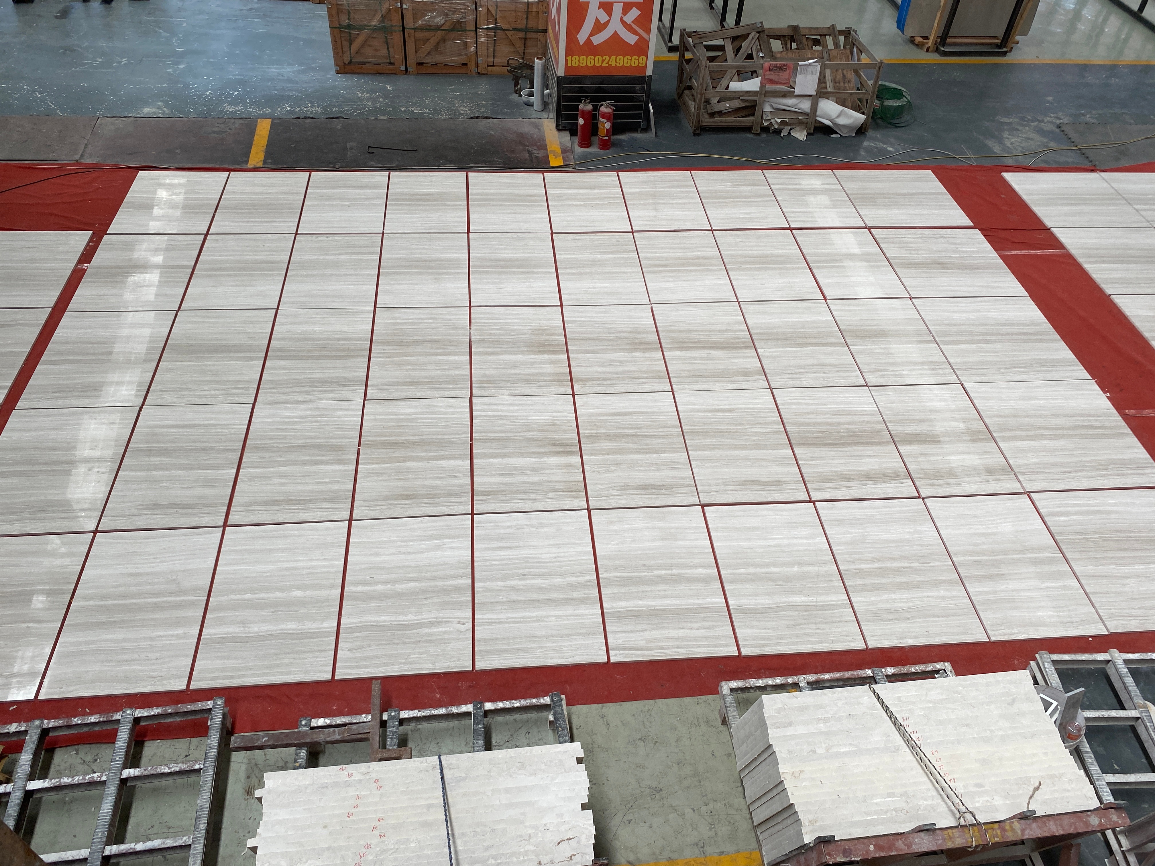 Overhead view of Sandalwood Light white wood marble tiles laid out in a grid on red film for quality inspection