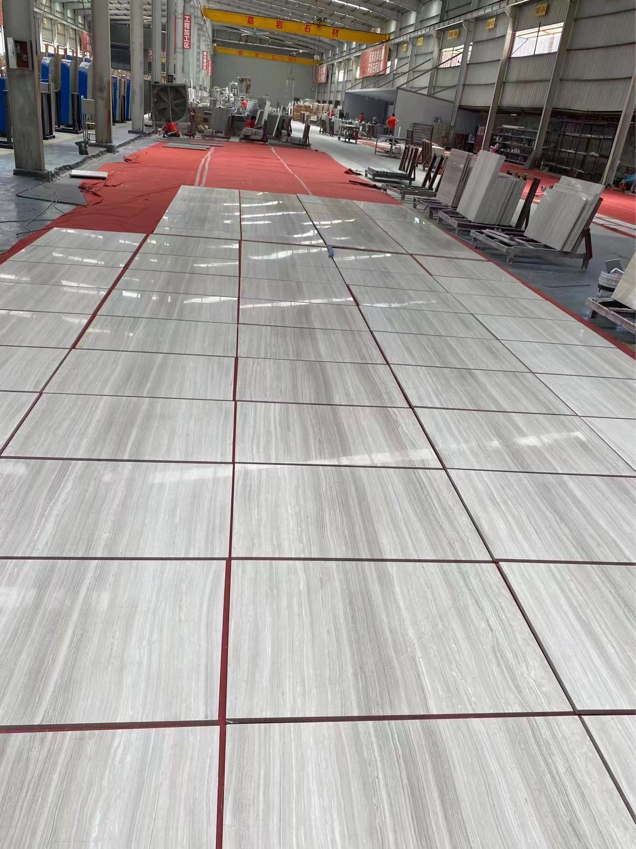 Polished Sandalwood Light white wood-vein marble tiles dry-laid down a factory aisle with marble slabs stacked alongside