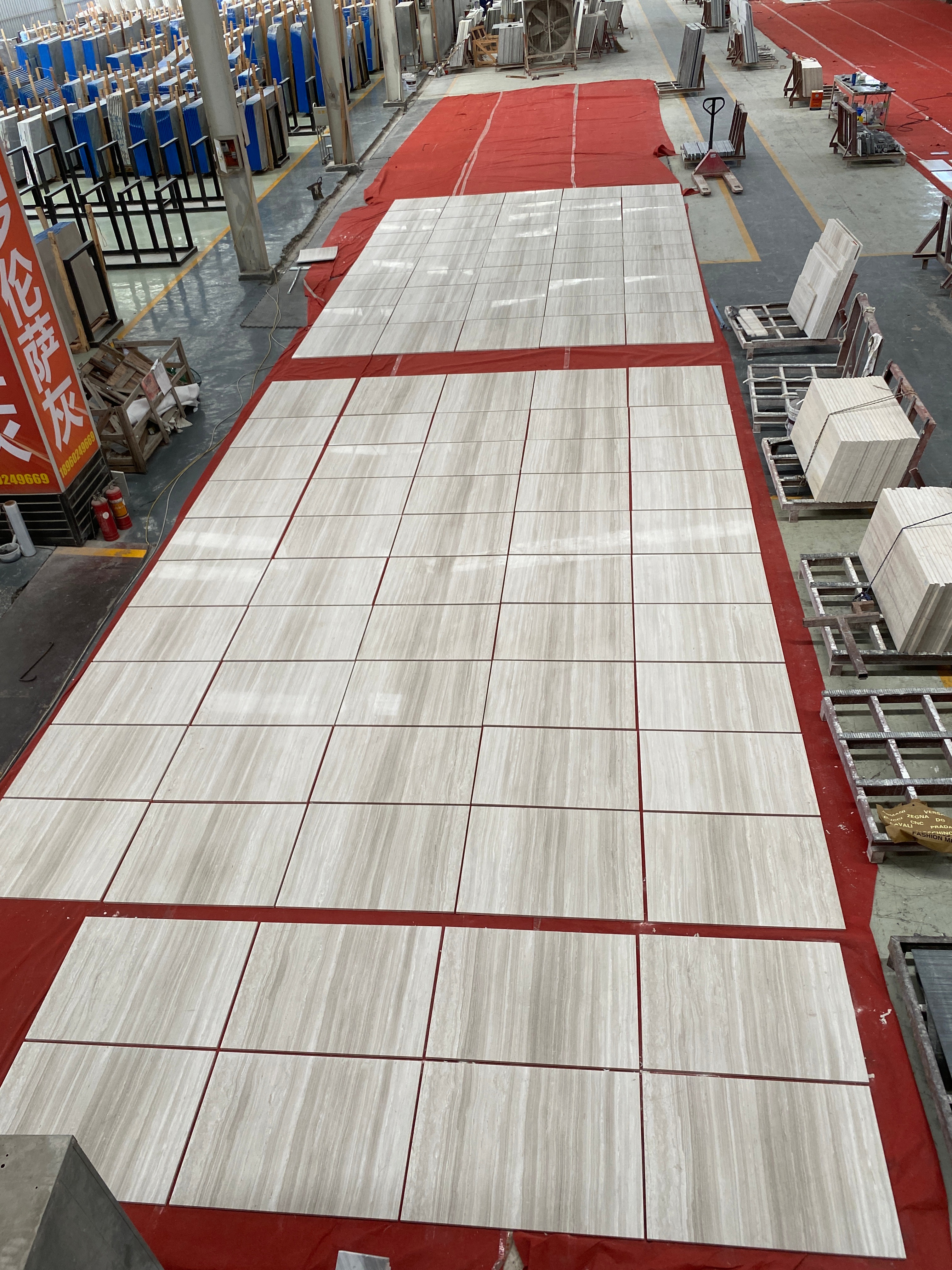 Large batch of Sandalwood Light white wood-vein marble tiles dry-laid in rows on red protection film for inspection at the factory