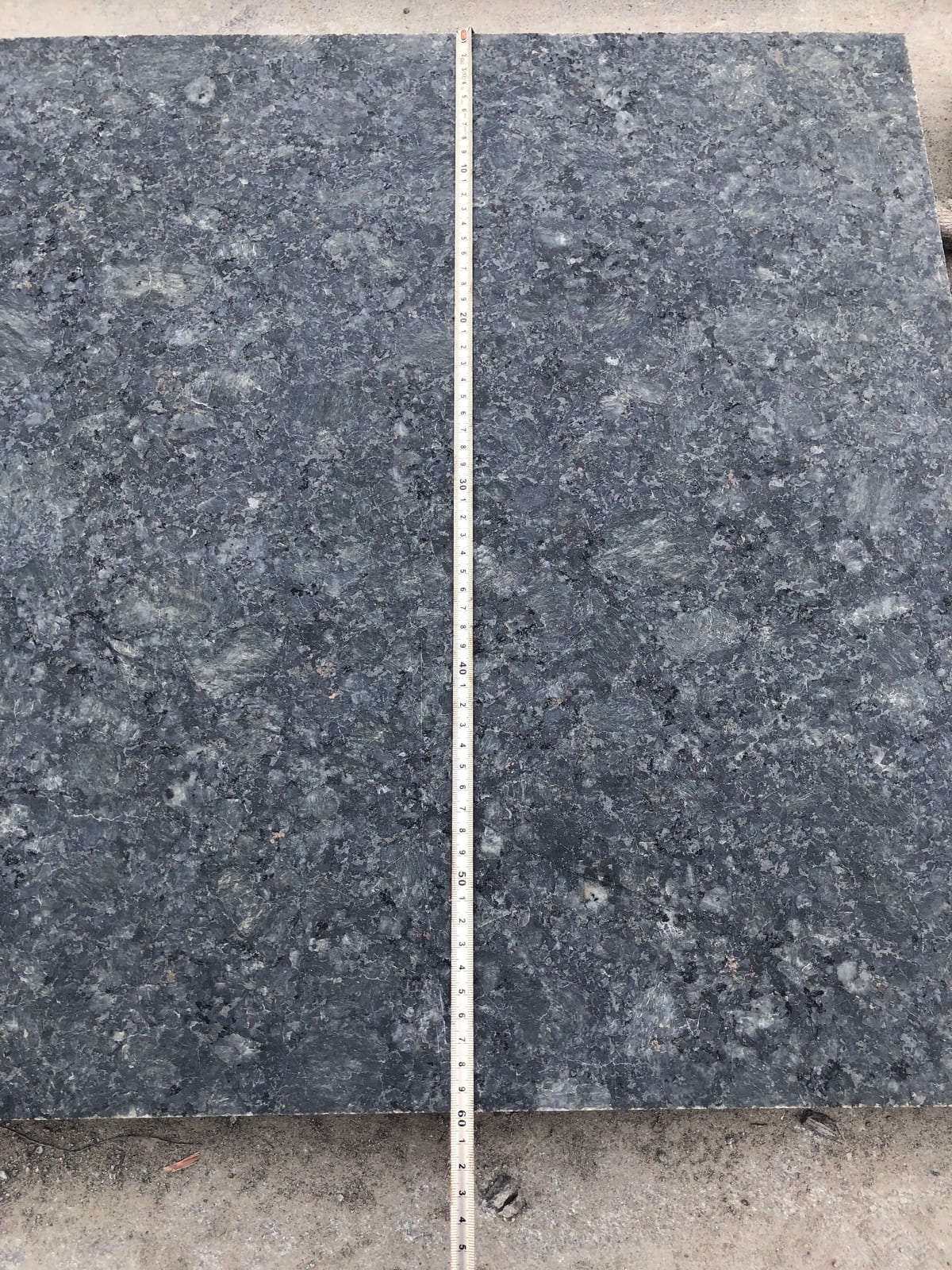 Long tape measure laid down the length of two dark Butterfly Green granite tiles
