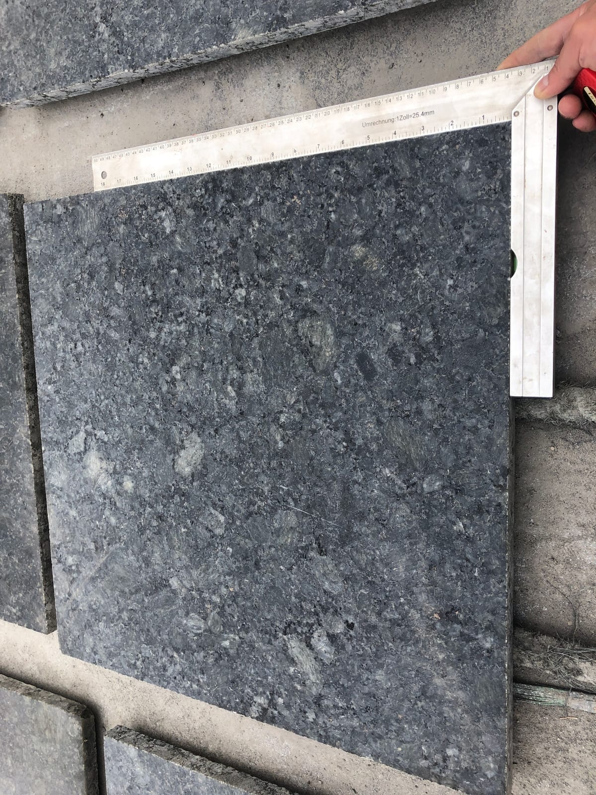 Carpenter square and ruler used to check the corner of a dark Breton Green granite tile