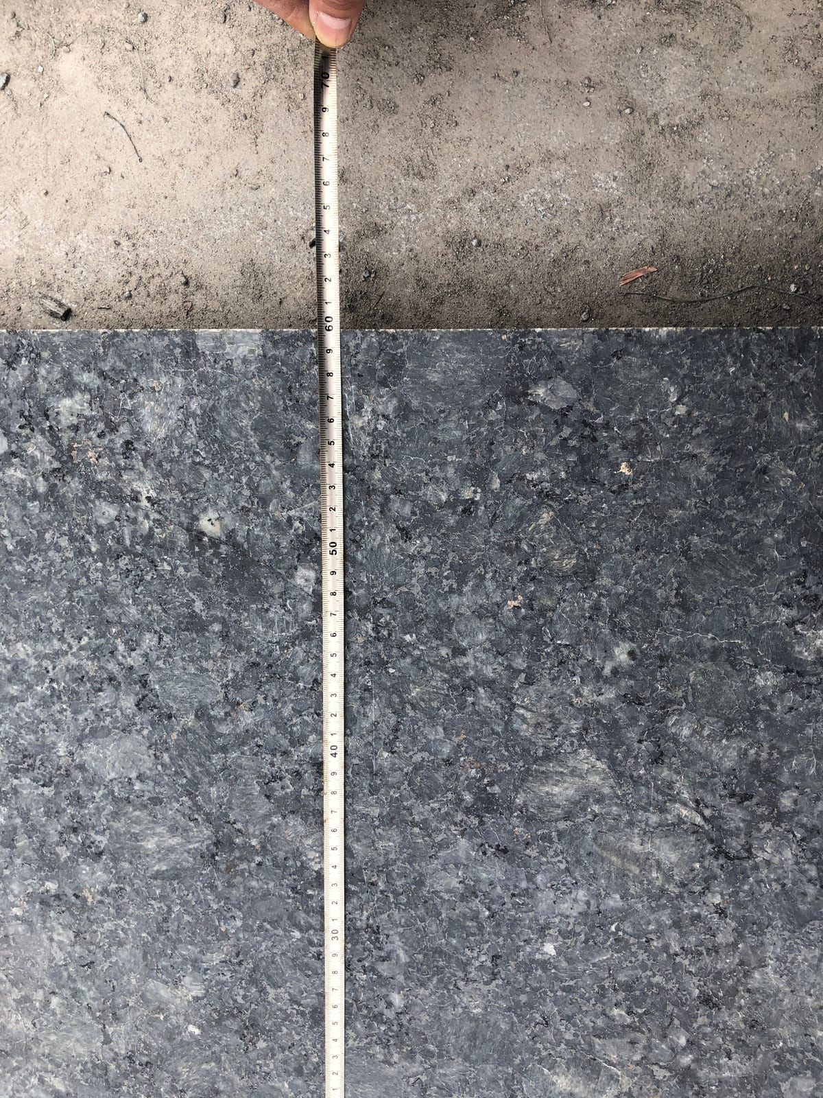 Tape measure checking the thickness and size of a dark Butterfly Green granite tile