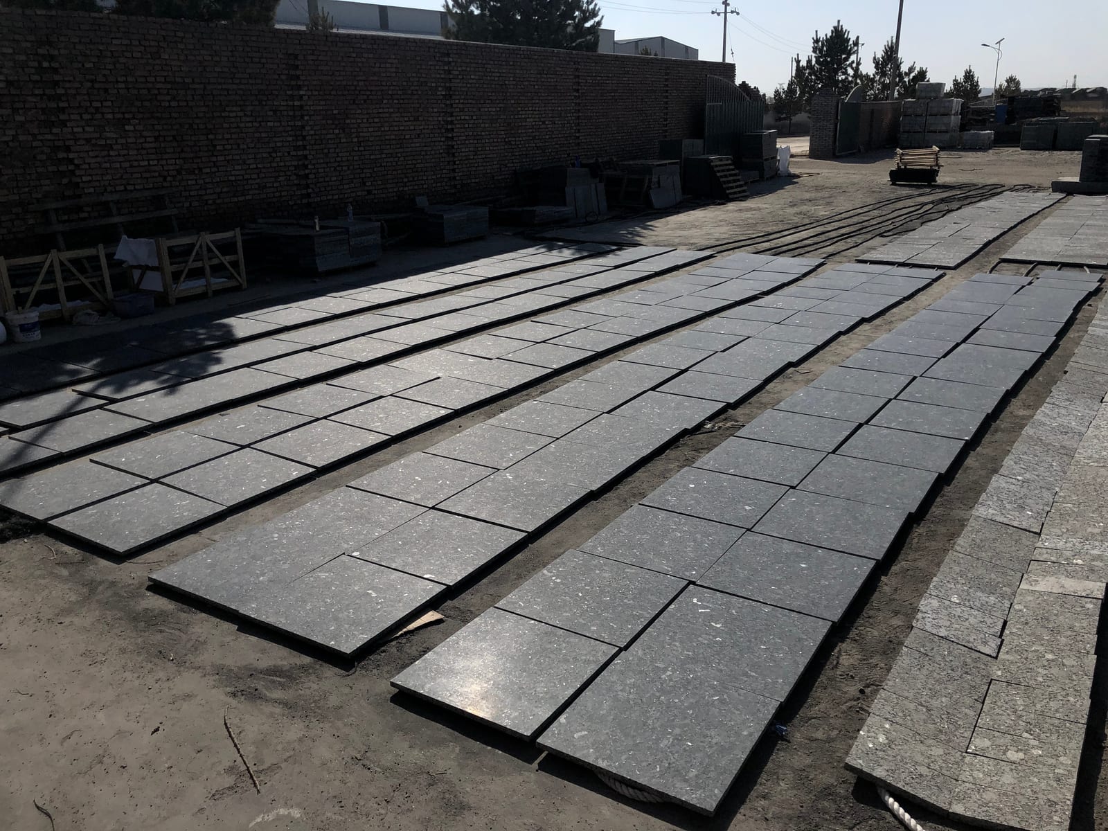 Wide view of dark Butterfly Green granite tiles drying in rows across a factory yard