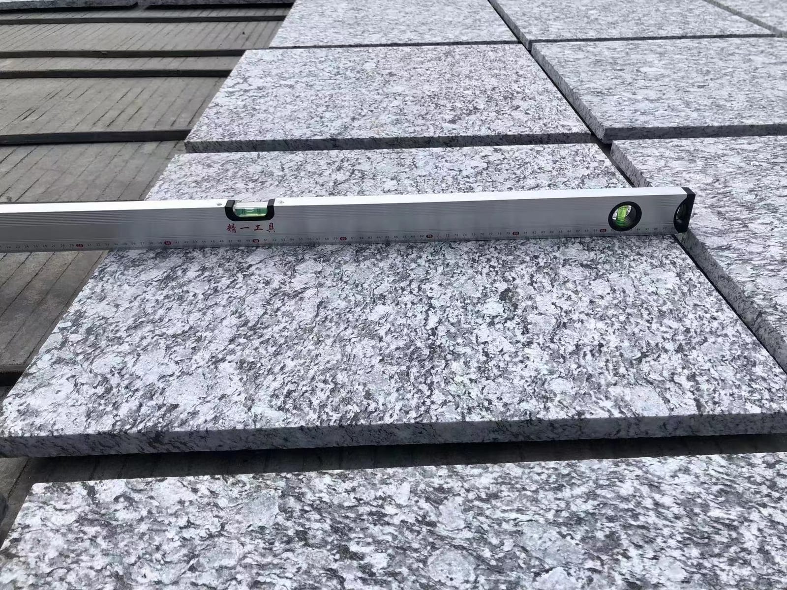 Spirit level laid across a sea-wave grey granite tile to check surface flatness