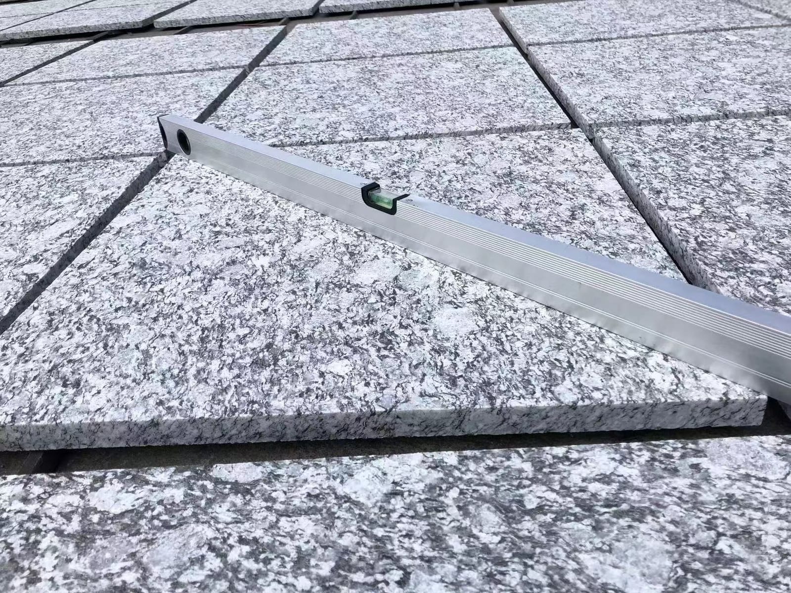 Aluminium spirit level resting on light grey granite tiles to verify flatness
