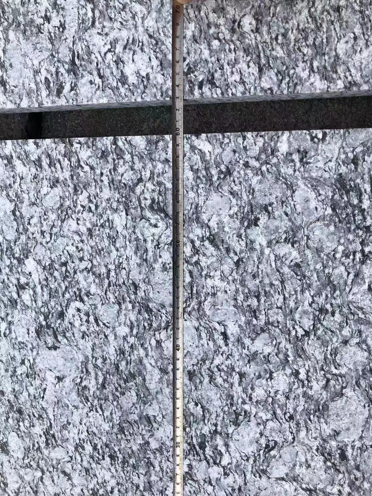 Folding ruler laid across two sea-wave pattern grey granite tiles to check module size