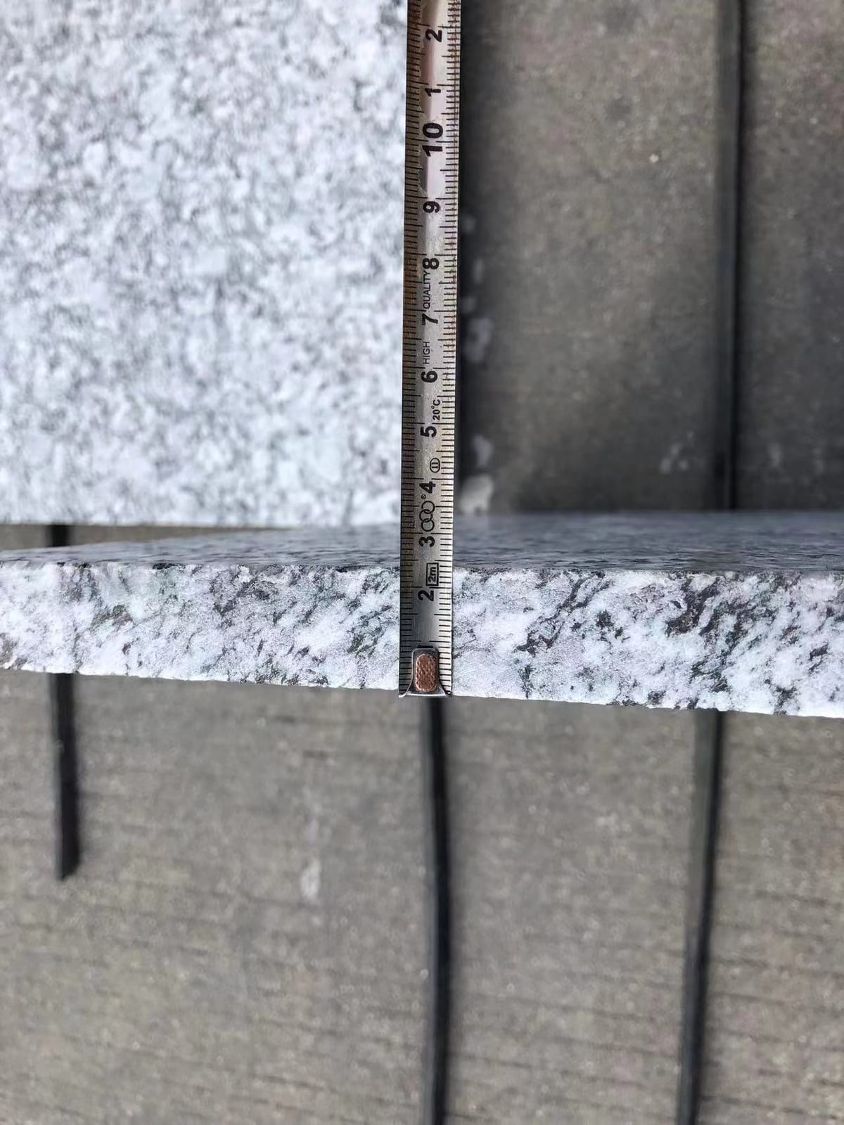 Tape measure checking the edge thickness of a sea-wave grey granite tile