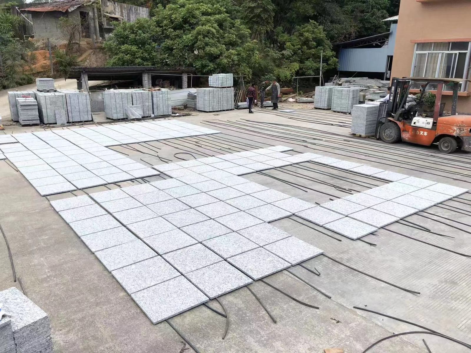 Large field of light grey granite tiles laid out flat to dry in the factory yard