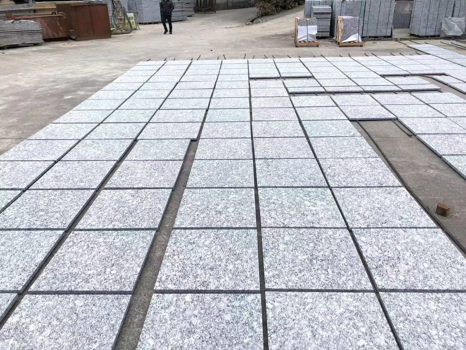 Wide view of light grey granite tiles drying in rows across the factory yard