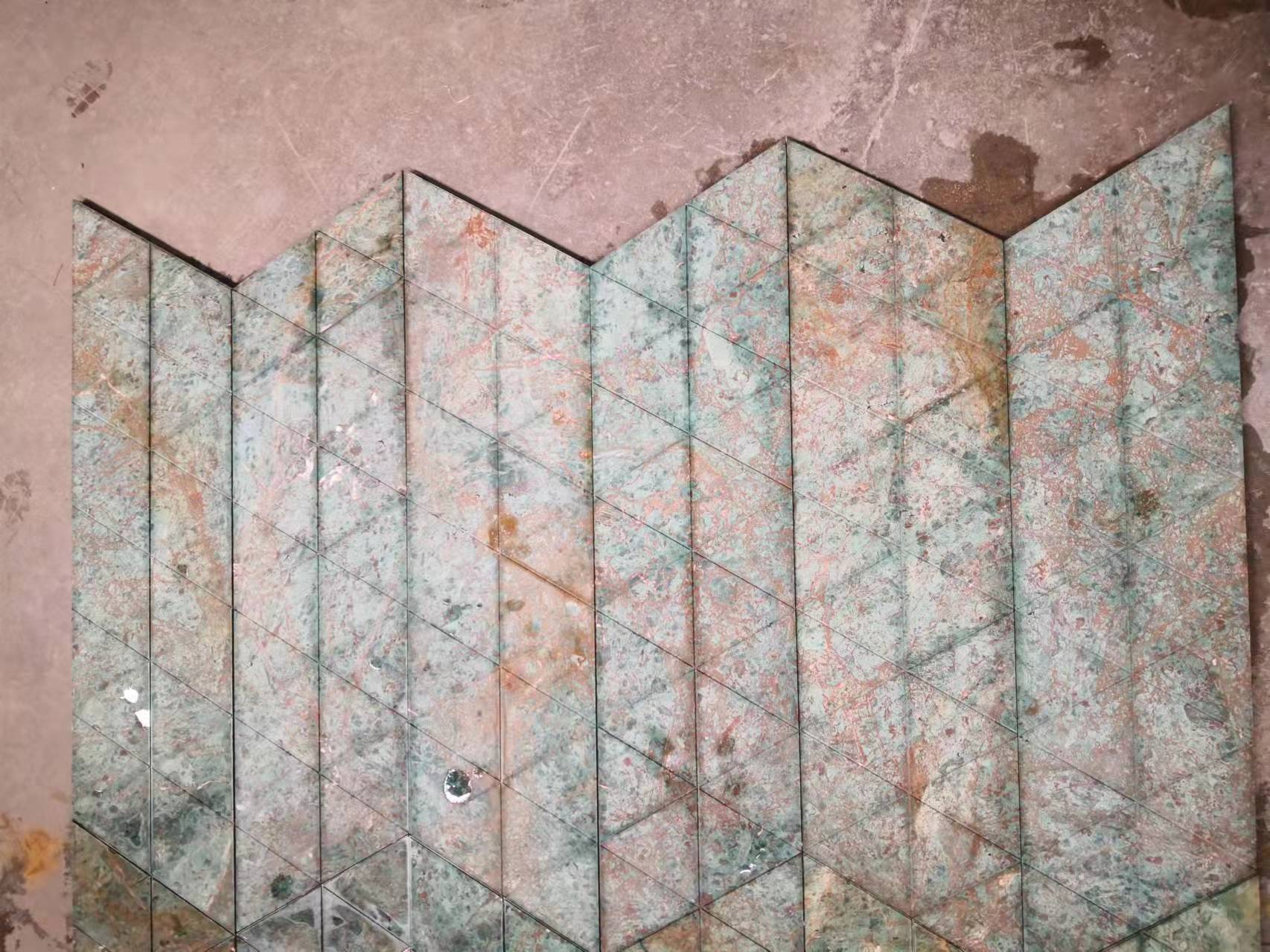 Triangular fluted green marble tiles forming a continuous chevron zigzag, seam-matched on the workshop floor