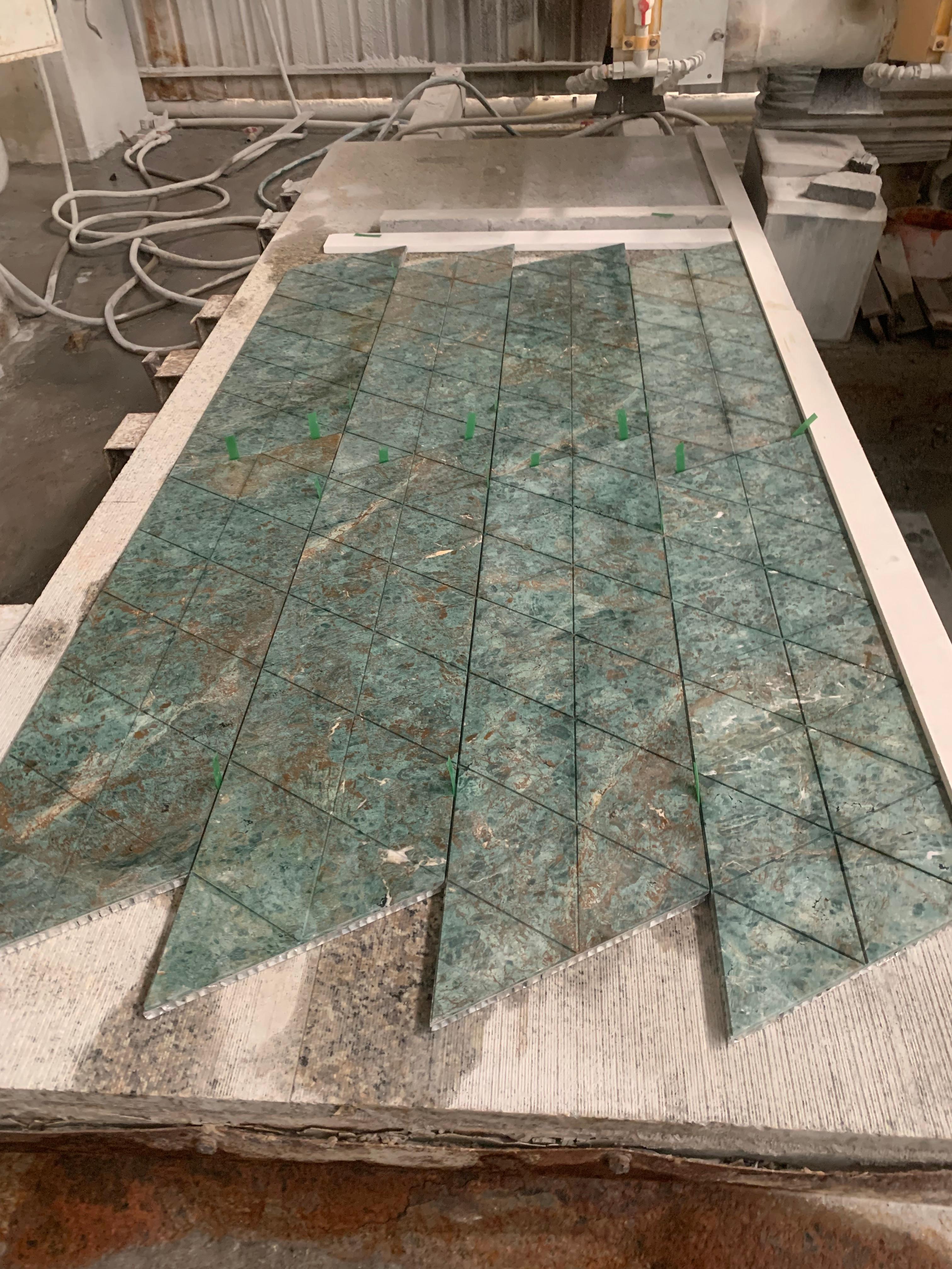 Triangular fluted Rainforest Green marble tiles arranged into chevron tips on the bridge-saw cutting table