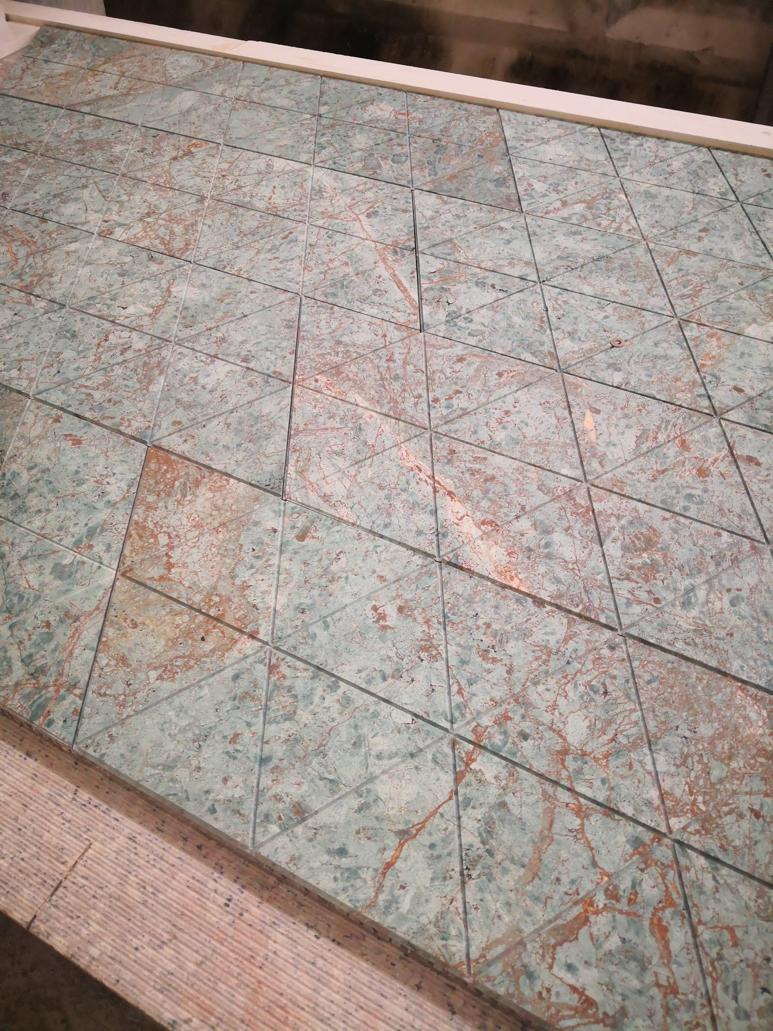 Overhead view of a triangular green marble tile grid being inspected for groove continuity