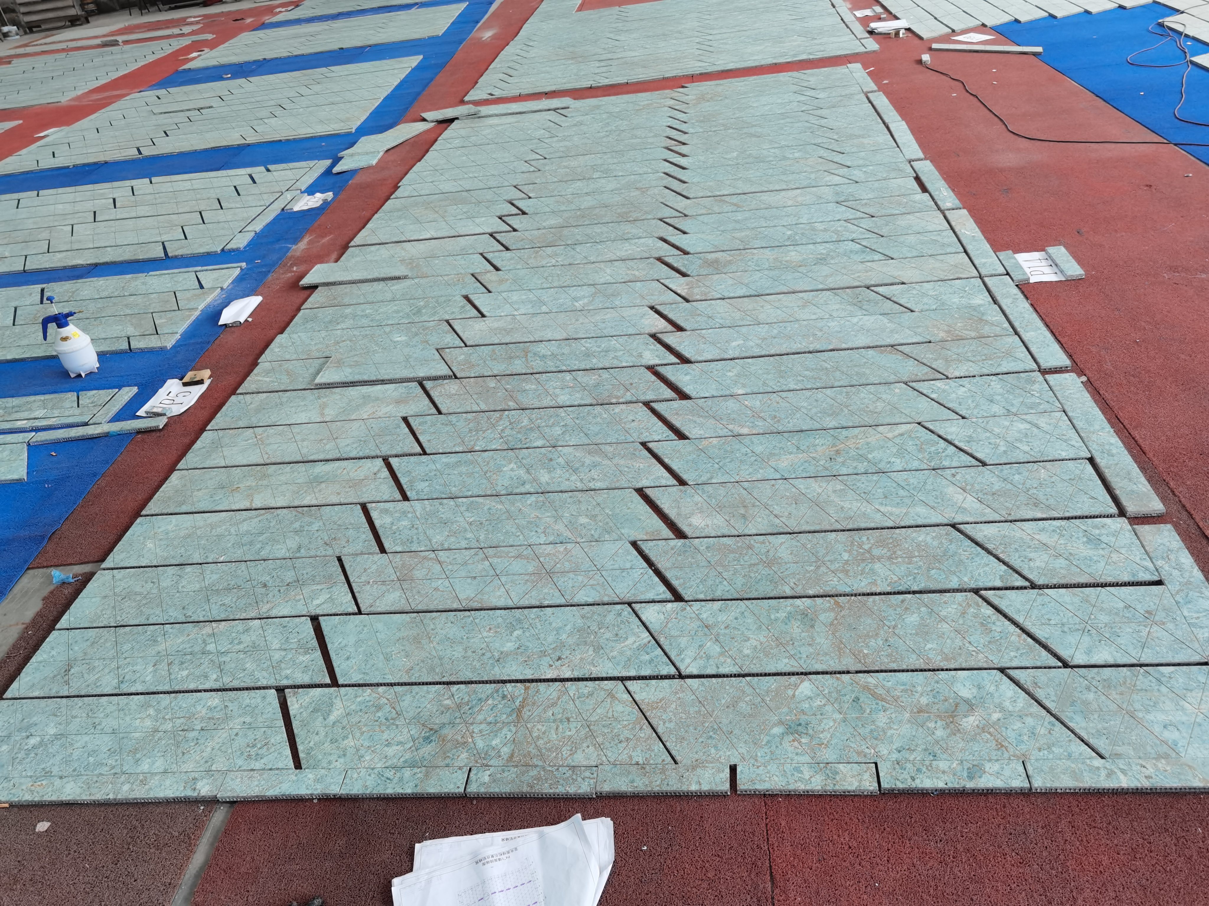 Wide factory dry-lay of the Studio City II triangular green marble floor pattern
