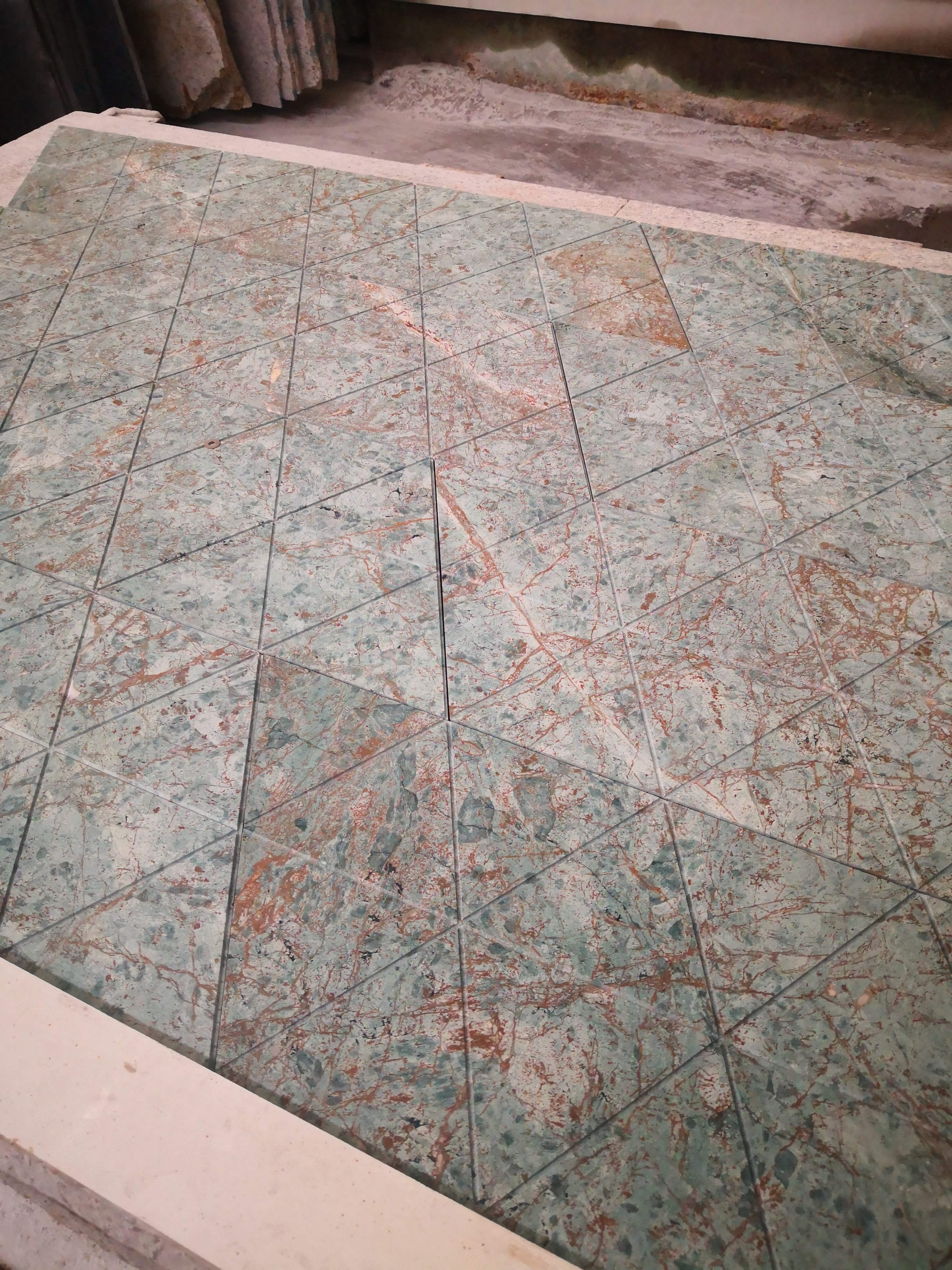 Triangular green marble tiles dry-laid on a white inspection frame for quality control