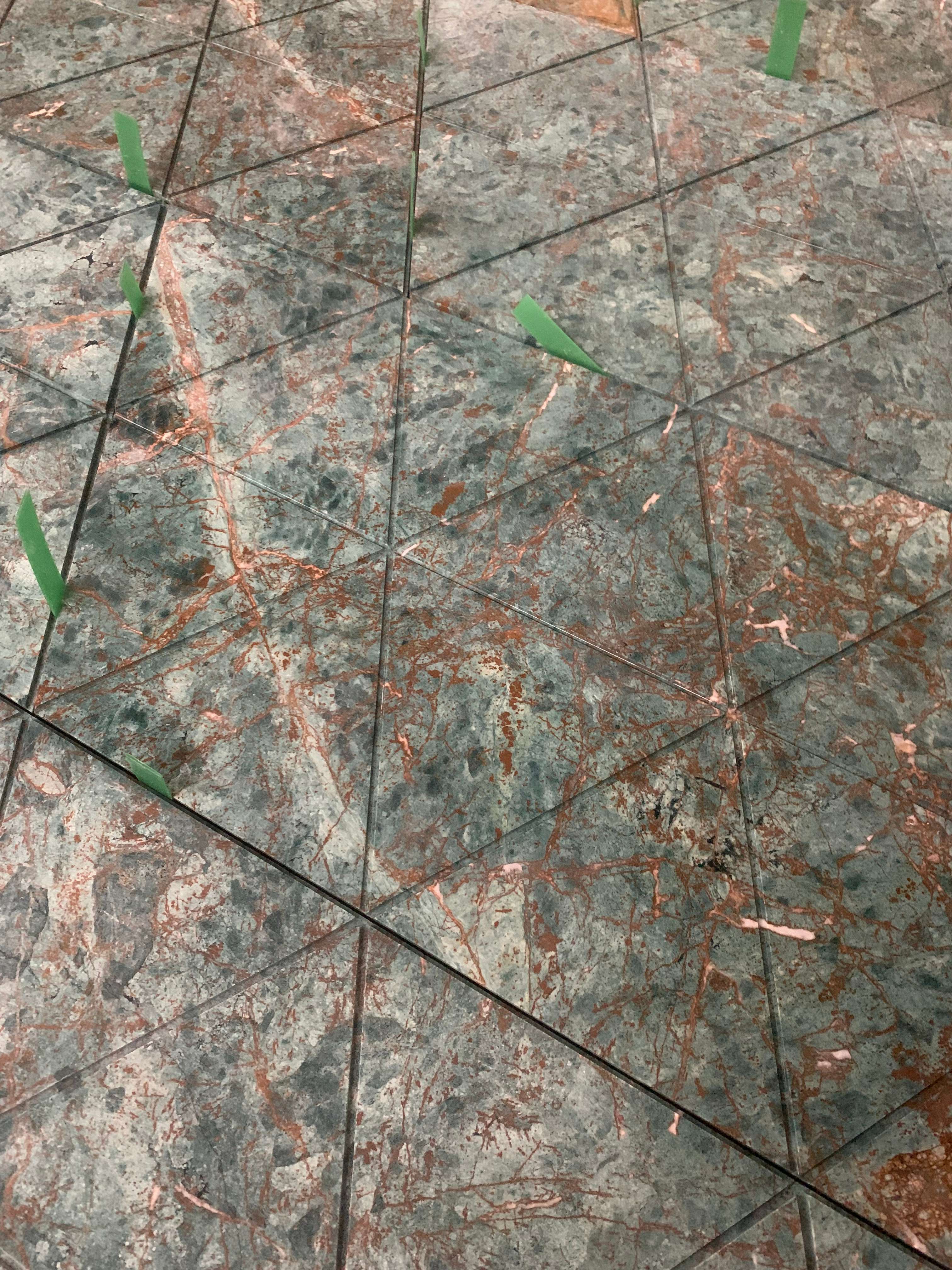 Angled close-up of triangular green marble seams being checked for alignment with green markers
