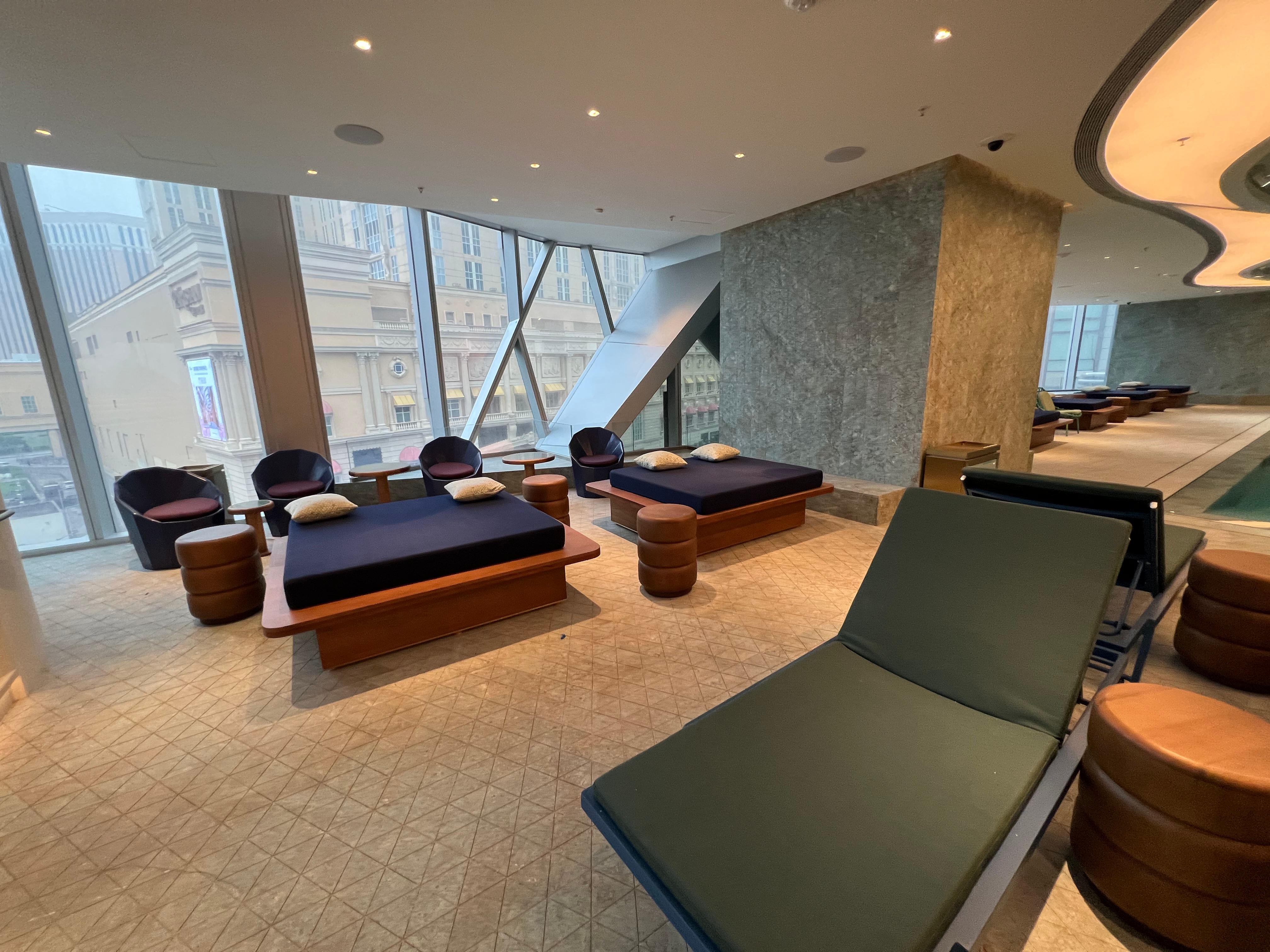 Spa lounge at Studio City II Macau with daybeds, floor-to-ceiling windows over the Cotai skyline and a green marble feature wall and triangular stone floor