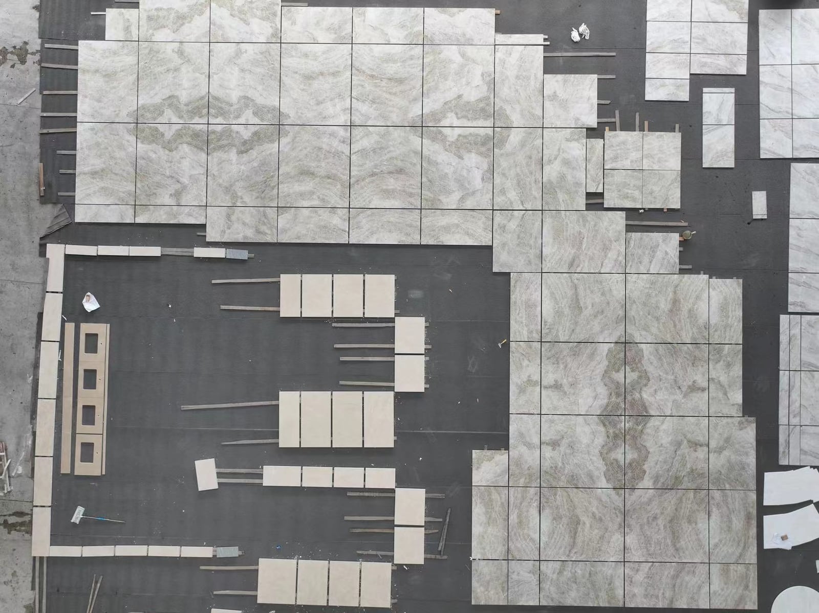 Overhead view of book-matched veined marble tiles dry-laid on the factory floor, matching the pre-cut plan exactly